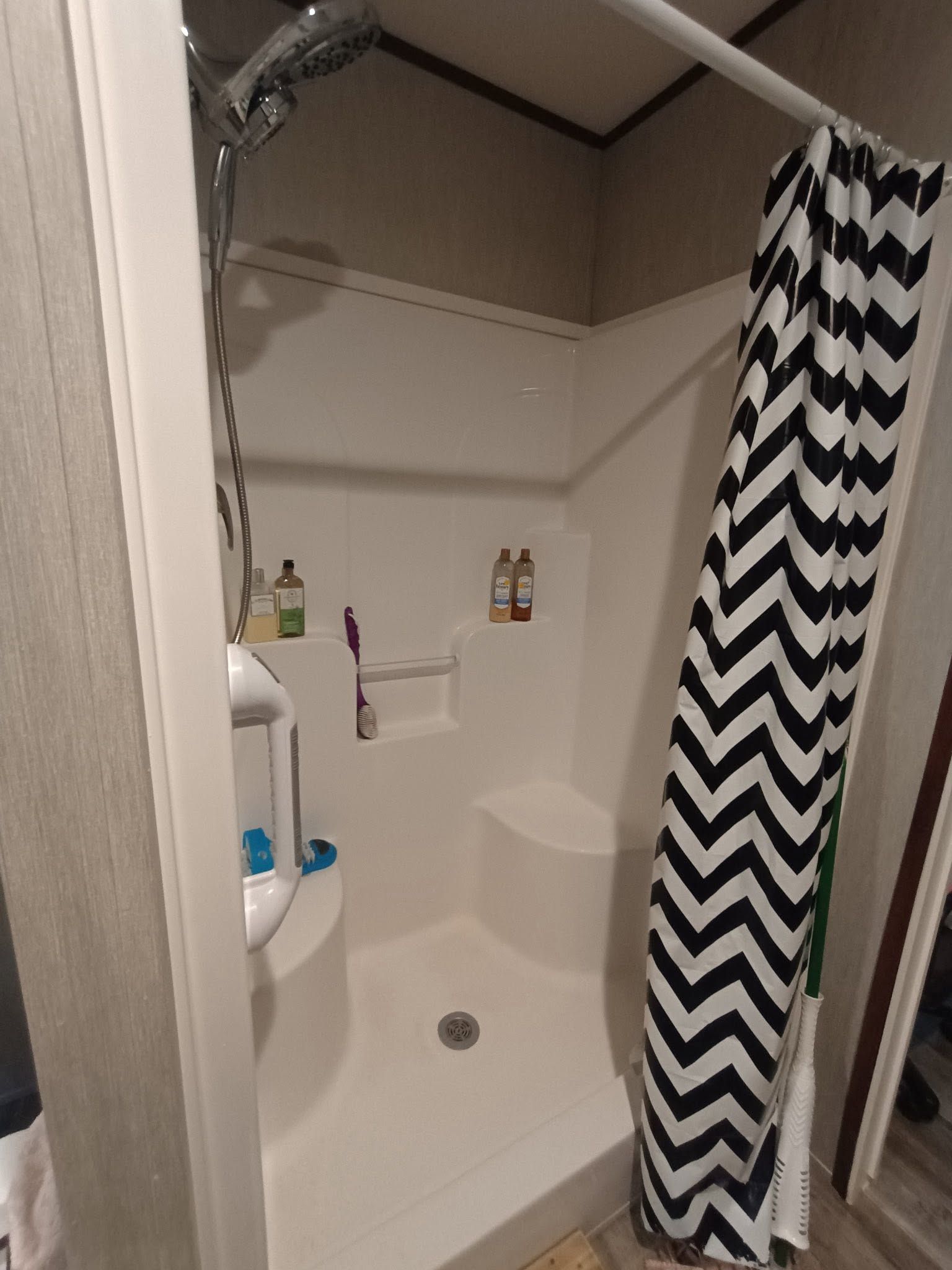 Small bathroom with a shower stall, black-and-white chevron curtain, and built-in shelf toiletries