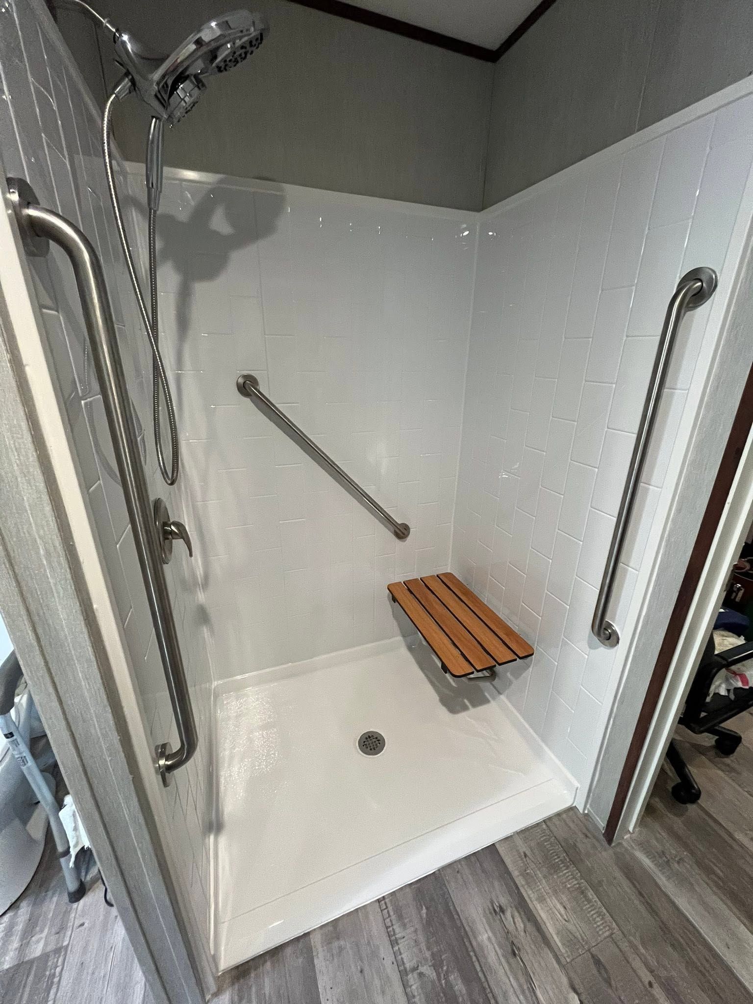 Accessible shower stall with grab bars, handheld shower, and fold-down wooden seat