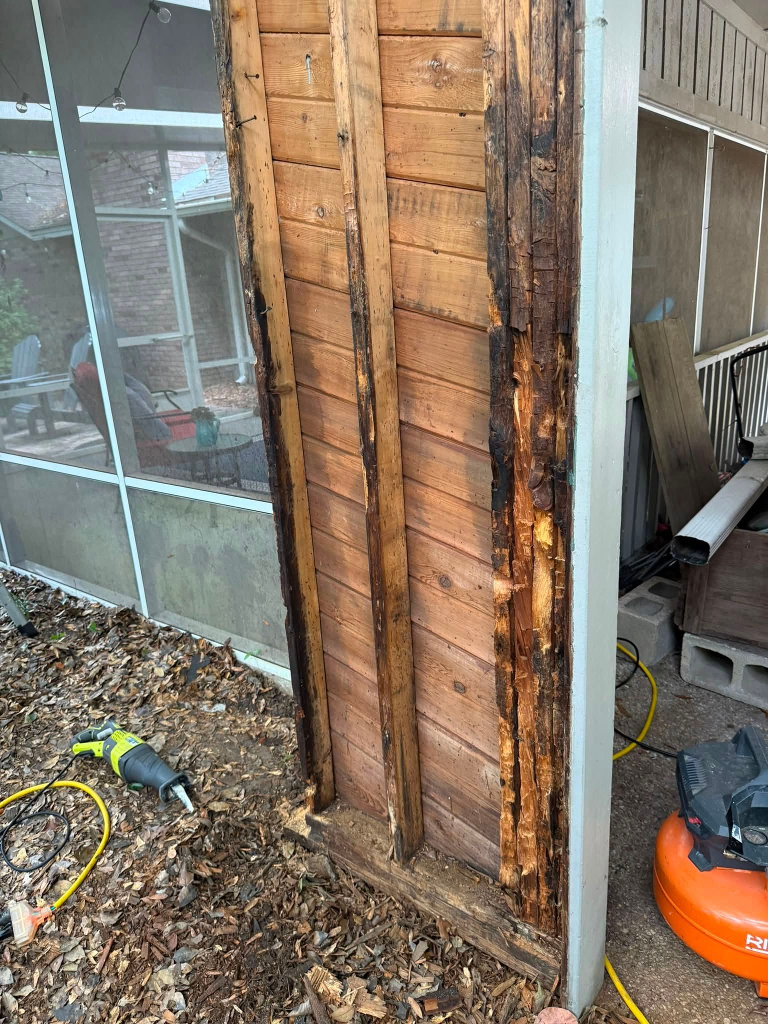 Exposed wooden wall corner with fire damage next to a window, with tools and an orange blower on the ground