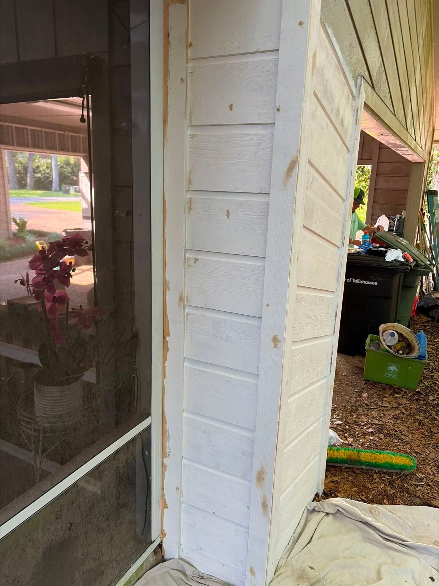 Porch corner with white siding beside a screened door, showing a garden area and toys in the background