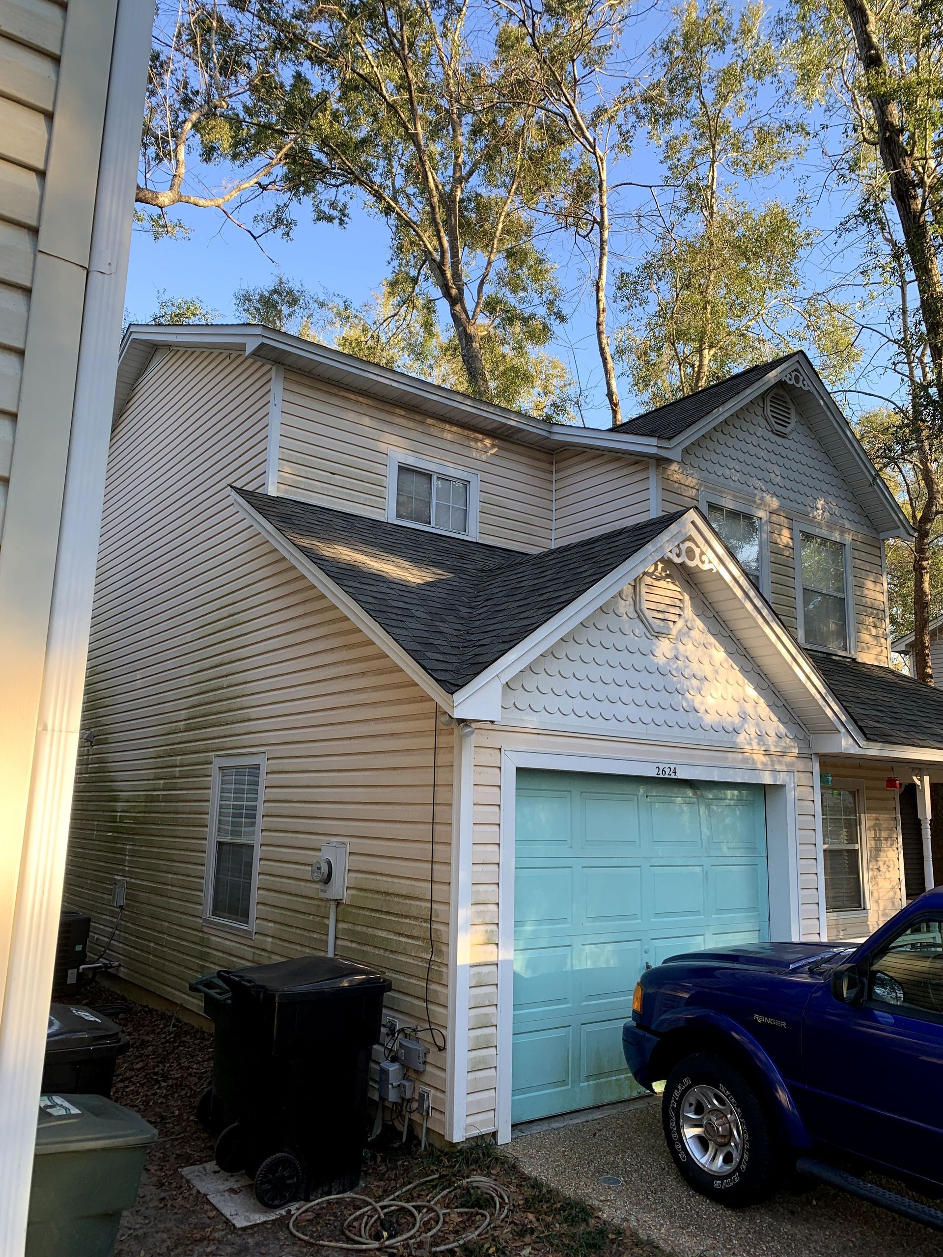 Suburban townhouse with a light blue garage door, tan siding, and a blue truck parked outside.