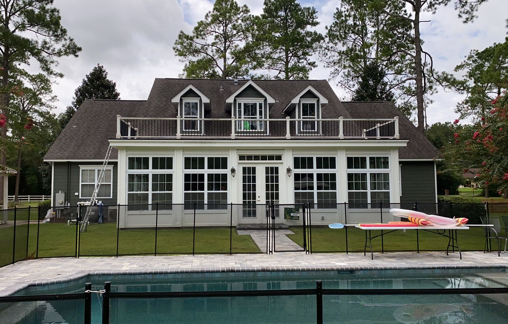 House with screened porch and dock beside a backyard pool, surrounded by tall trees.