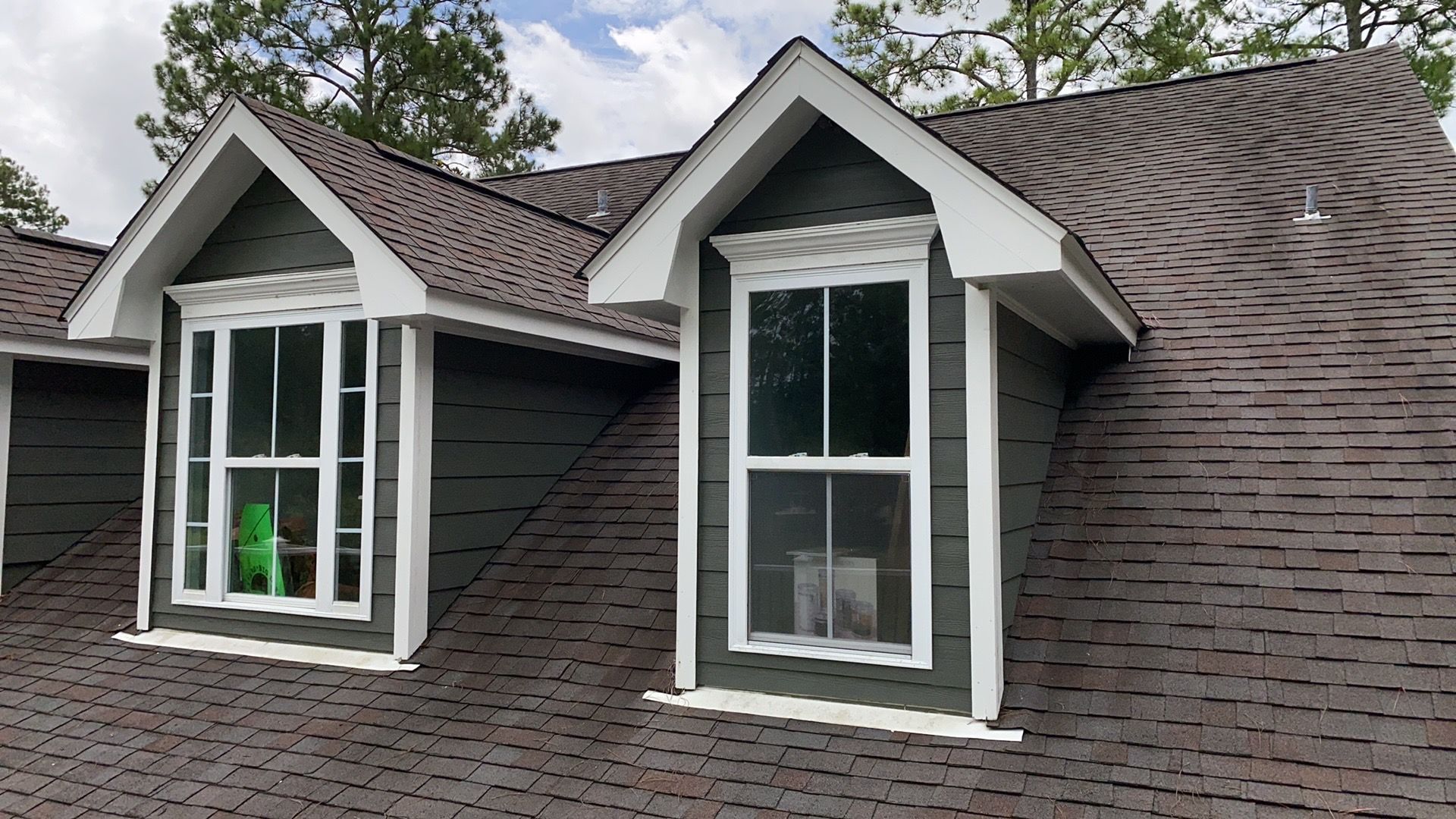 Two dormer windows with white trim on a dark gray shingled roof