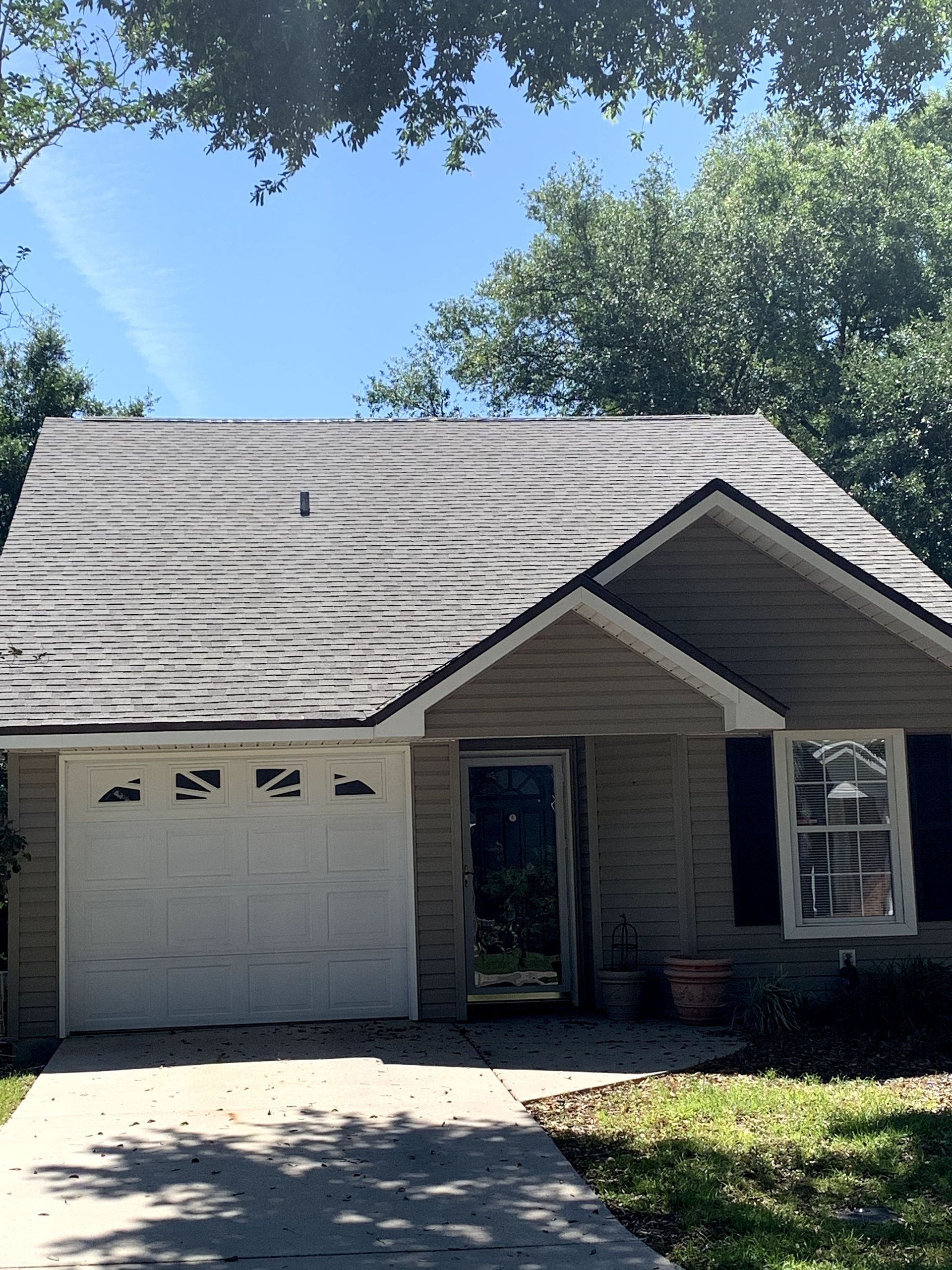Small house with gray roof, white garage door, and front porch under sunny trees.
