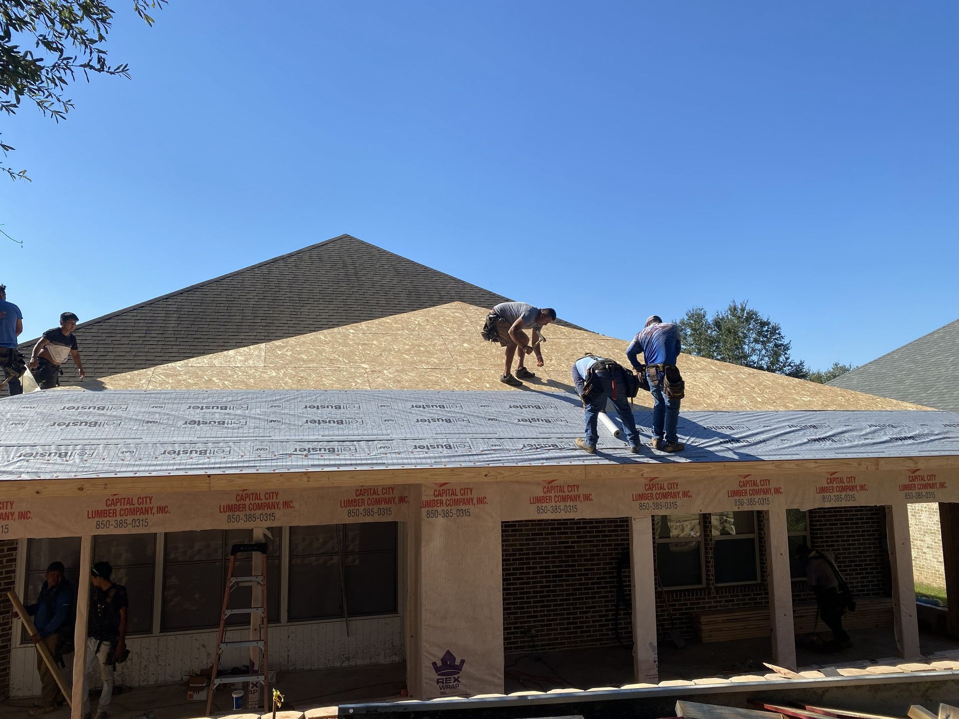 Workers roof a building with gray shingles under a clear blue sky.