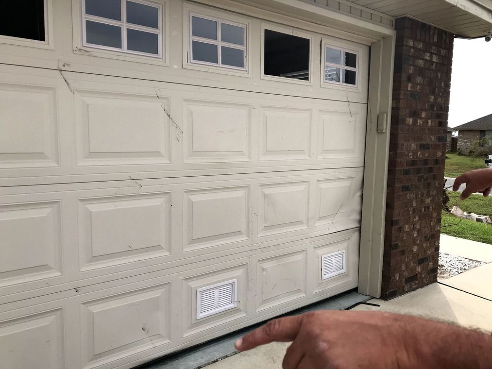 White garage door with decorative windows and brick trim, viewed from a driveway.