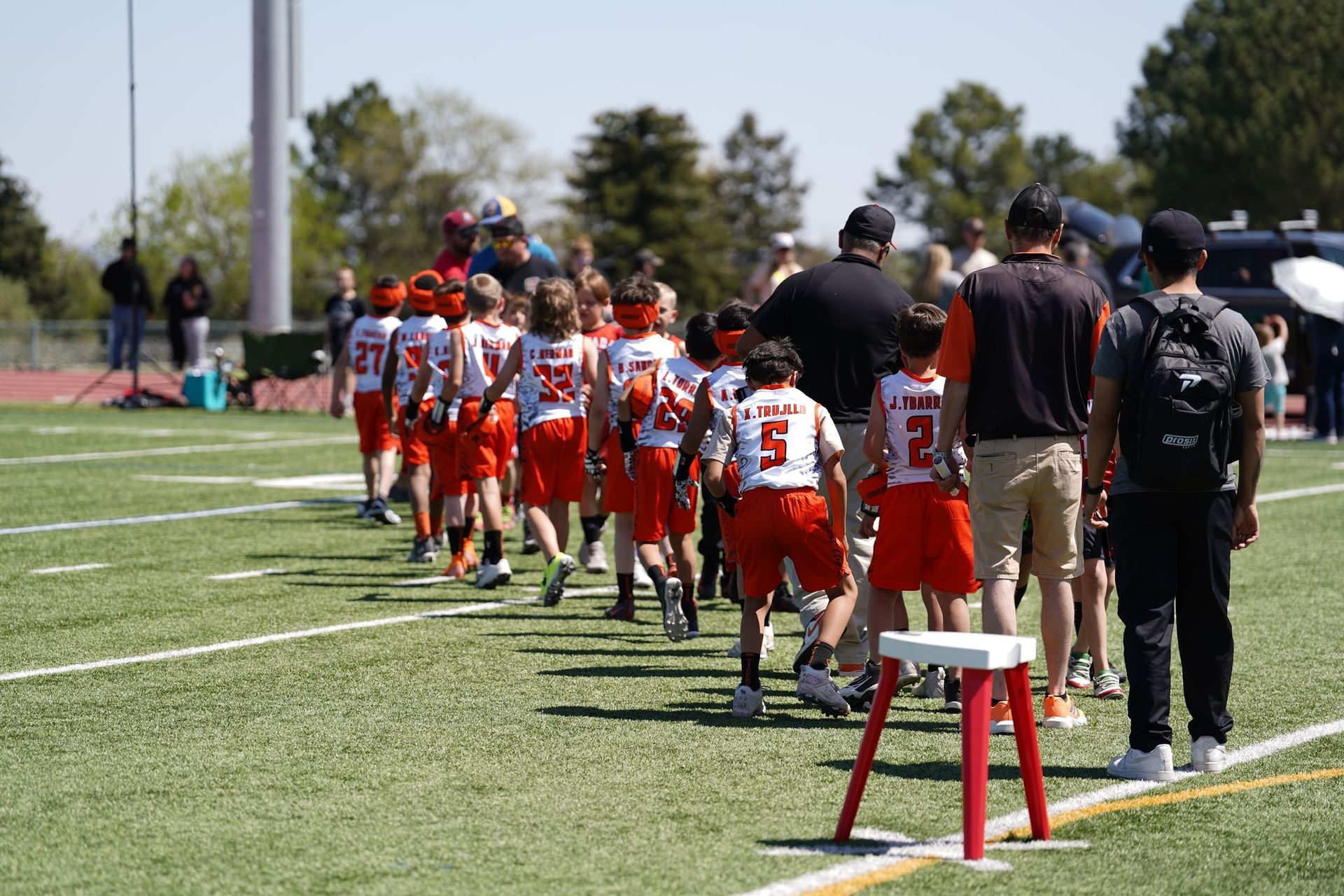 Youth football team in orange uniforms lined up on a sunny sideline during a game