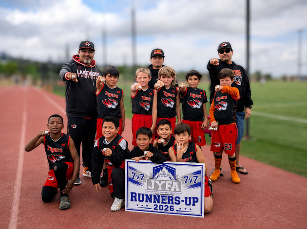 Youth baseball team posing on a field with a runners-up trophy sign, wearing black and red uniforms.