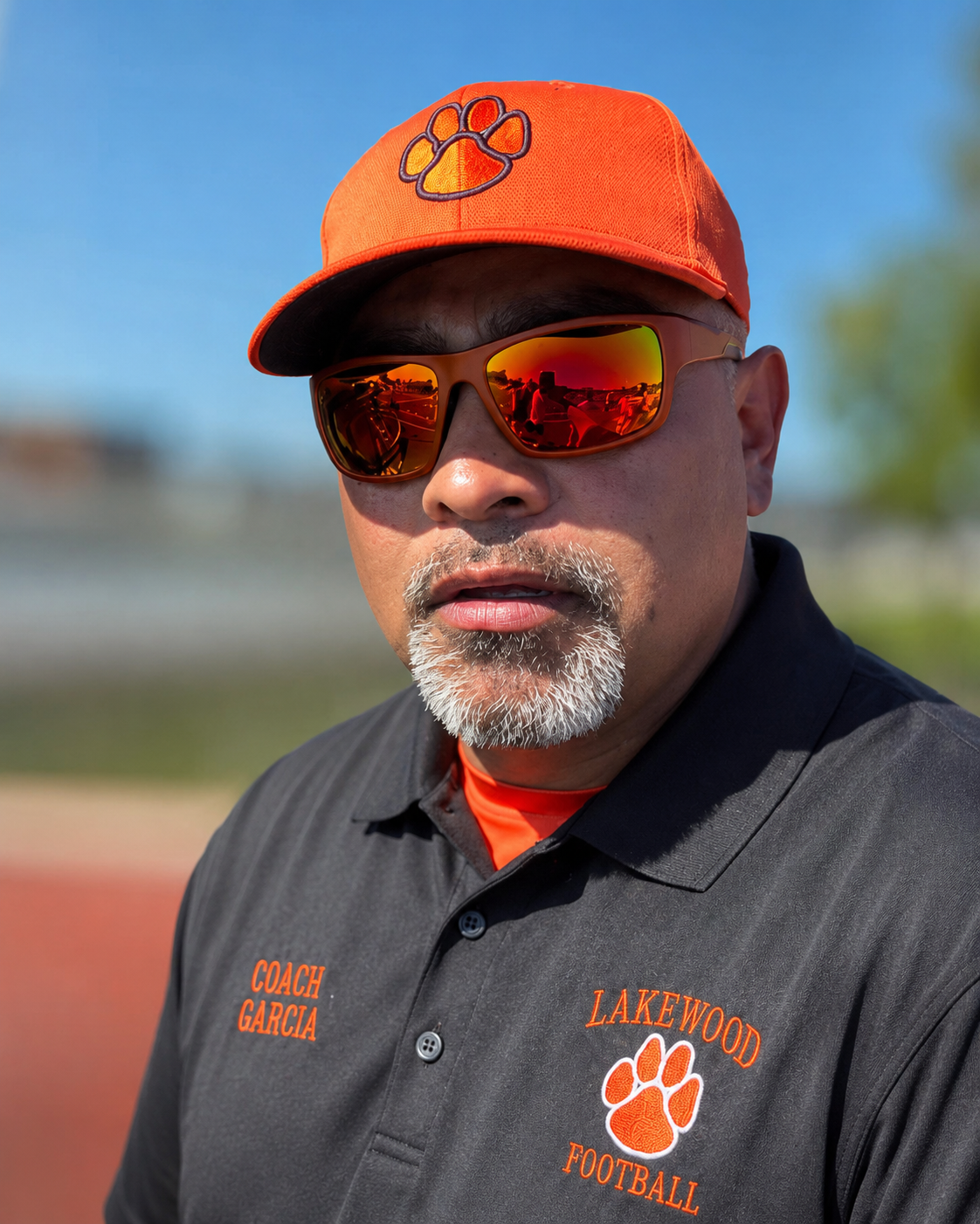 Man in orange cap and sunglasses wearing a black polo with orange logo, outdoors in sunlight