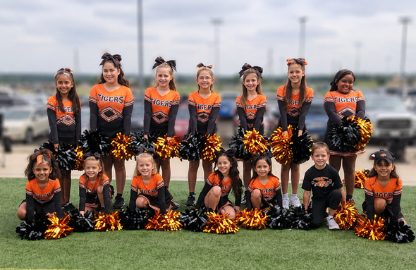 Youth cheer team posing in black and orange uniforms on a grassy field.