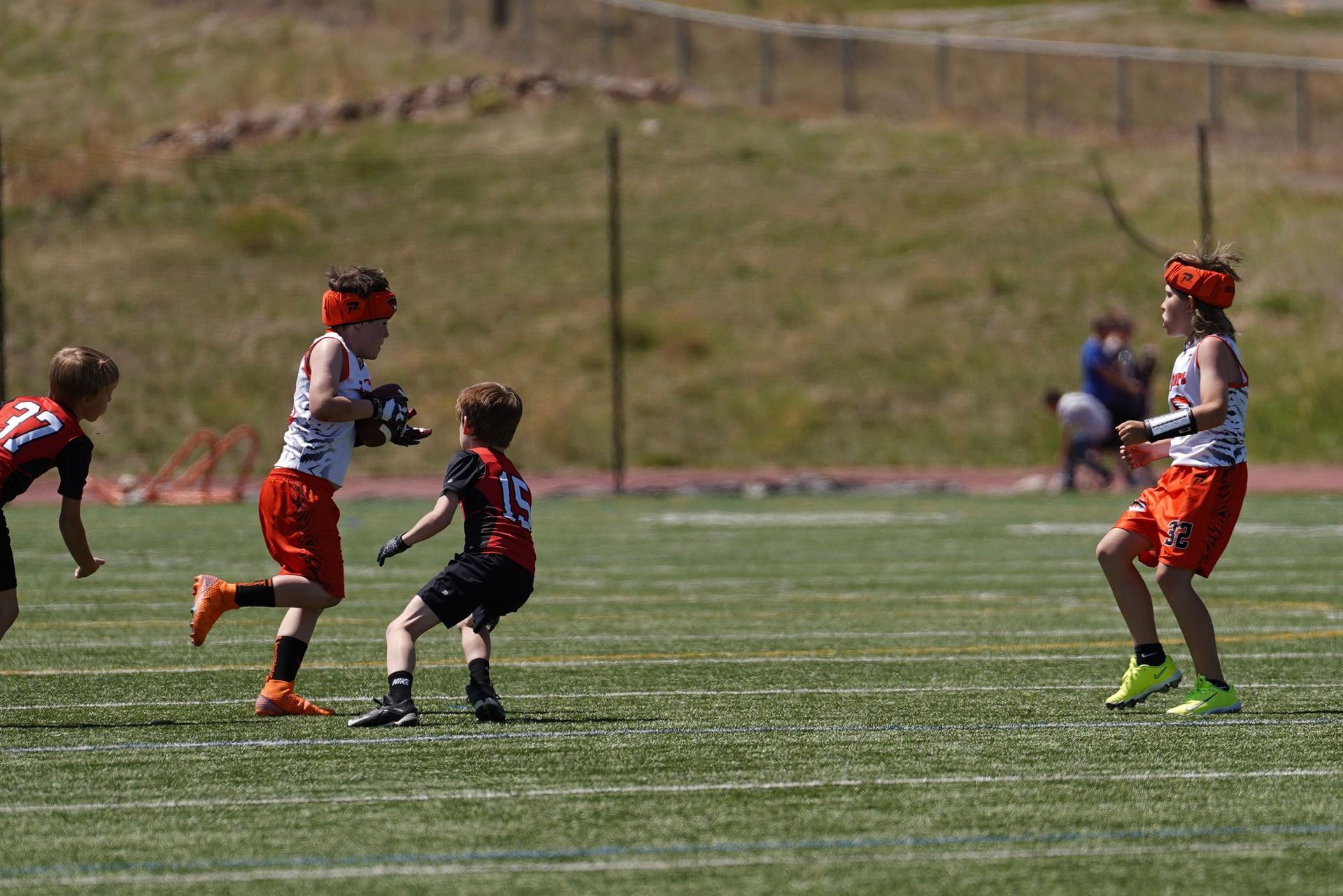 Youth lacrosse players in red and black uniforms running on a grassy field during a game