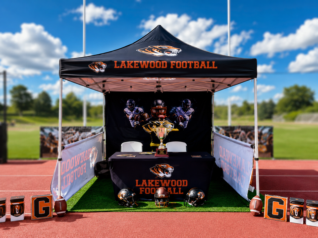 Lakewood Football trophy display tent on a track, with black and orange banners and trophies inside.