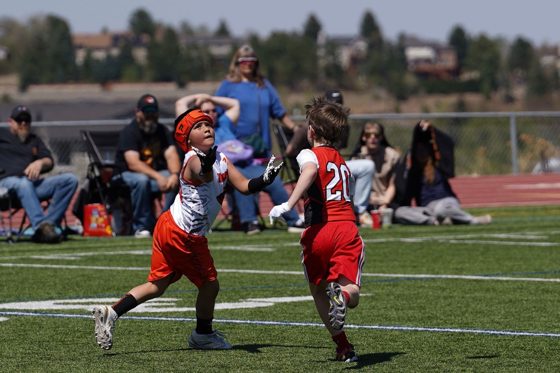 Two youth lacrosse players in red and white uniforms sprint and reach for the ball on a turf field