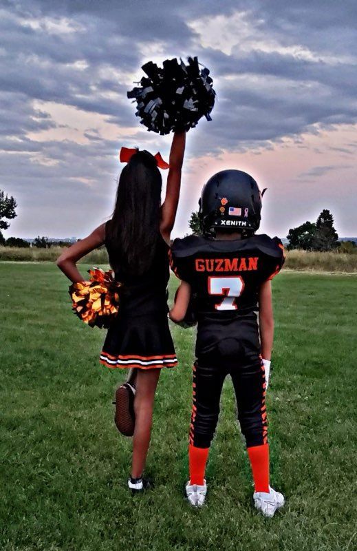 Cheerleader and football player holding pom-poms, standing on a field at sunset, seen from behind