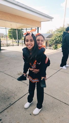 Woman in black outfit carrying a smiling child in a black-and-orange dress outdoors on a paved walkway.