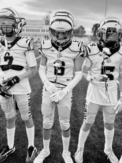 Three football players in white uniforms and helmets standing on a field, facing the camera.