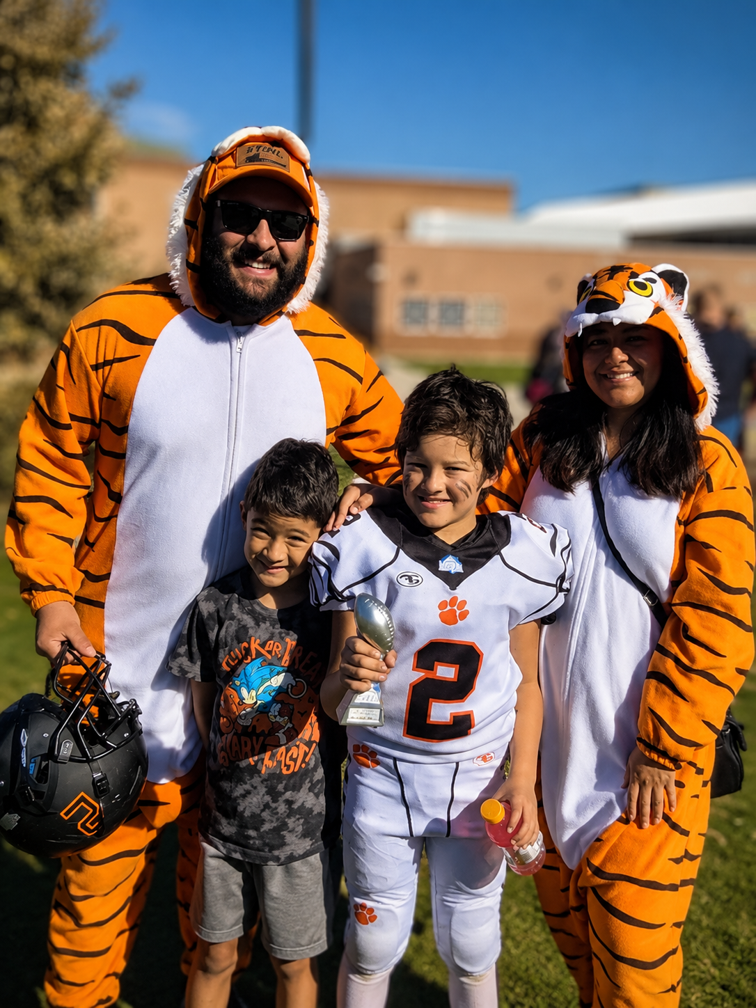 Family in tiger costumes and a football jersey posing outdoors on a sunny day
