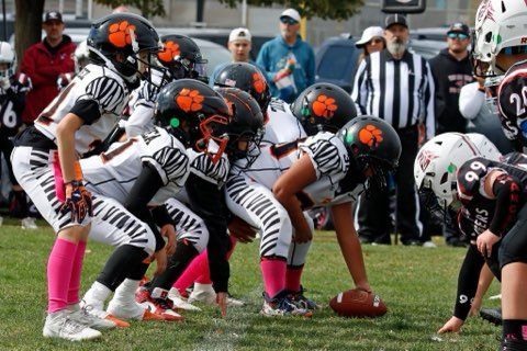 Youth football players lined up at the line of scrimmage on a grassy field, ready for the play