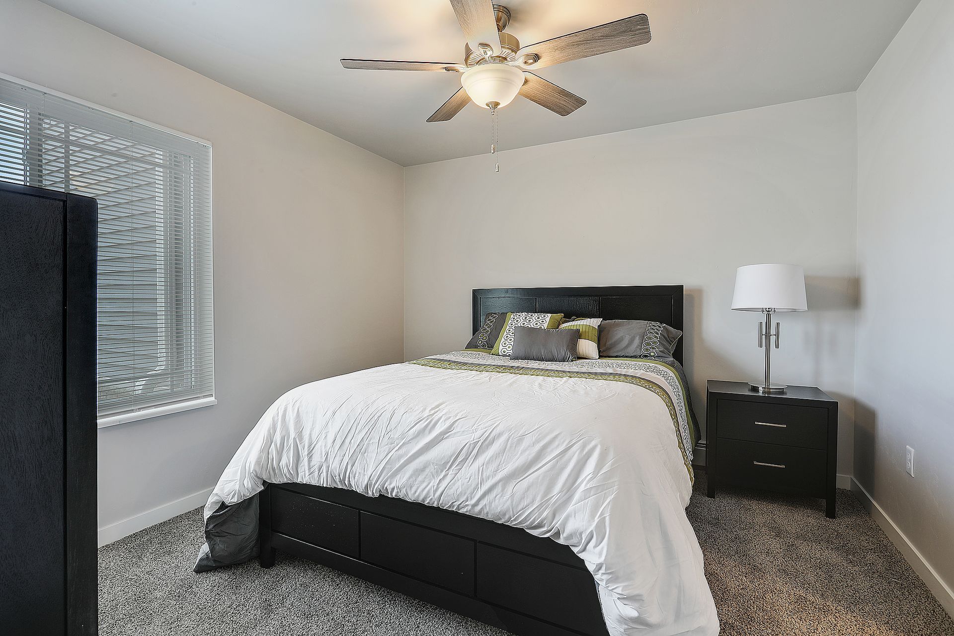 Neatly furnished bedroom with a bed, nightstand, lamp, window, and ceiling fan.