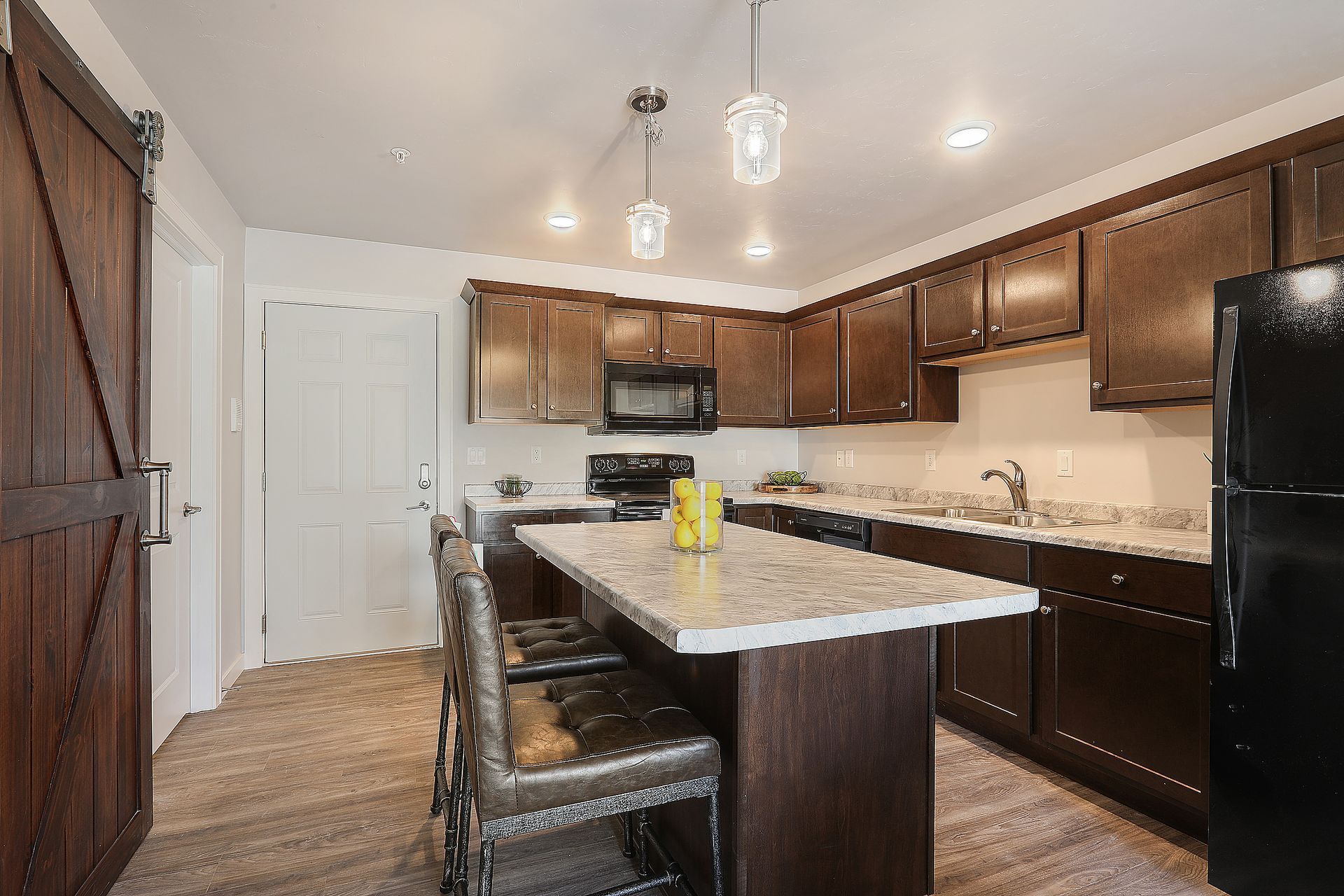Modern kitchen with dark wood cabinets, granite island, pendant lights, and black appliances