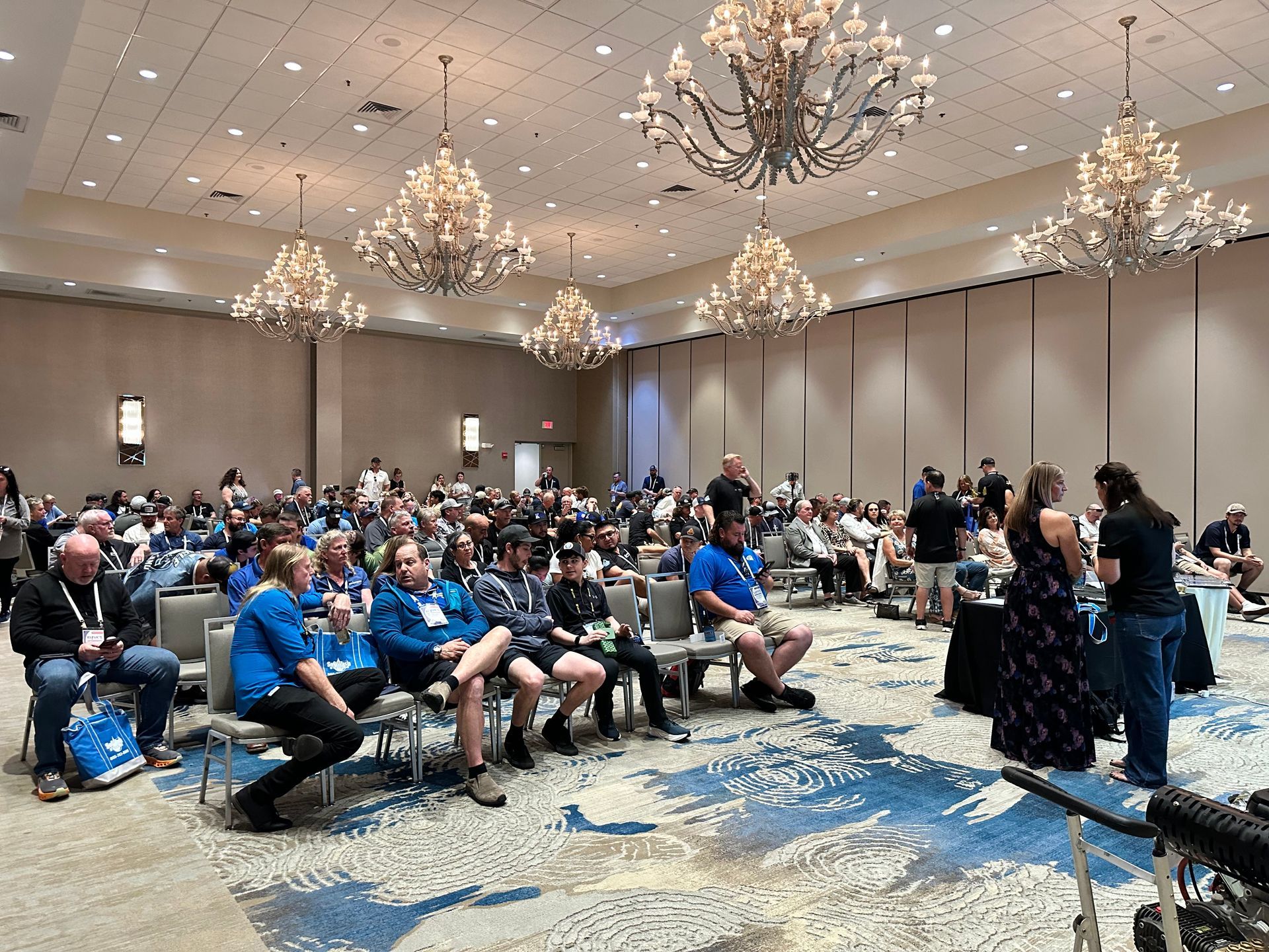 Conference audience seated in a ballroom under chandeliers, facing a presentation area.