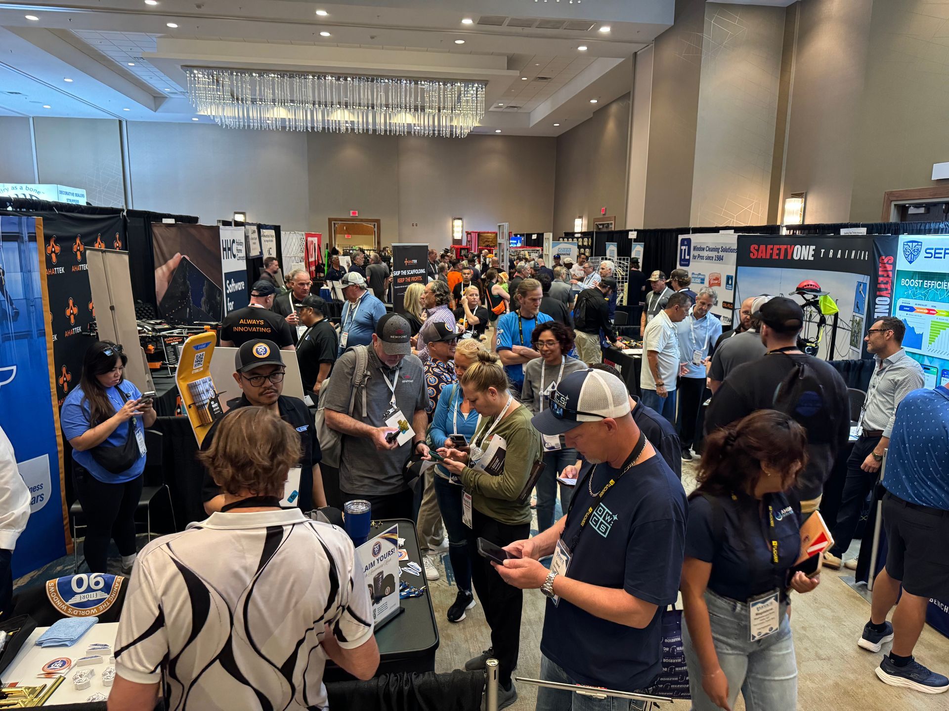 Crowded conference hall with booths, banners, and attendees browsing exhibits and talking