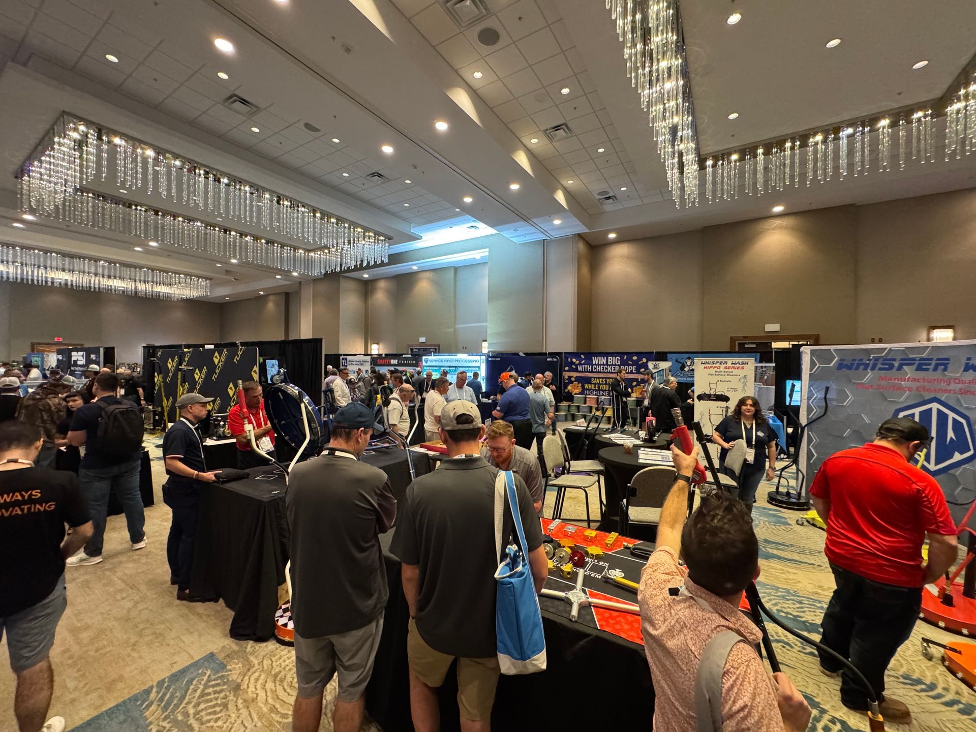 Crowded convention hall with vendor booths and attendees browsing displays under bright ceiling lights