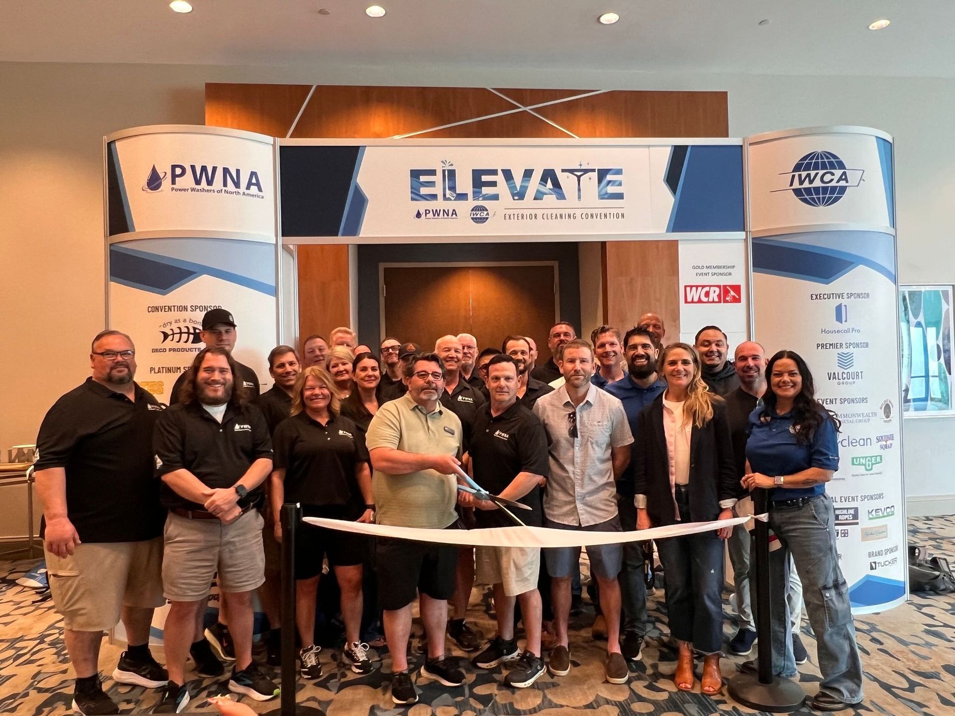 Group of people posing at the ELEVATE conference booth with a white table and blue-and-white banners