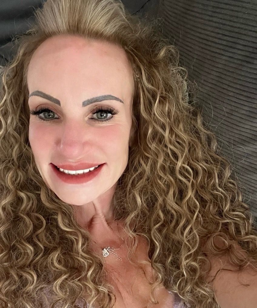 A man with a beard and sunglasses is standing in front of a car.