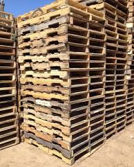 Stacks of weathered wooden pallets in a sunlit outdoor storage yard