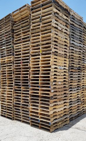 Stacked wooden pallets in a warehouse yard, forming a tall rectangular block.