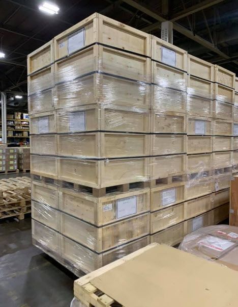 Stacked wooden crates wrapped in plastic in a warehouse, with a cardboard box in the foreground