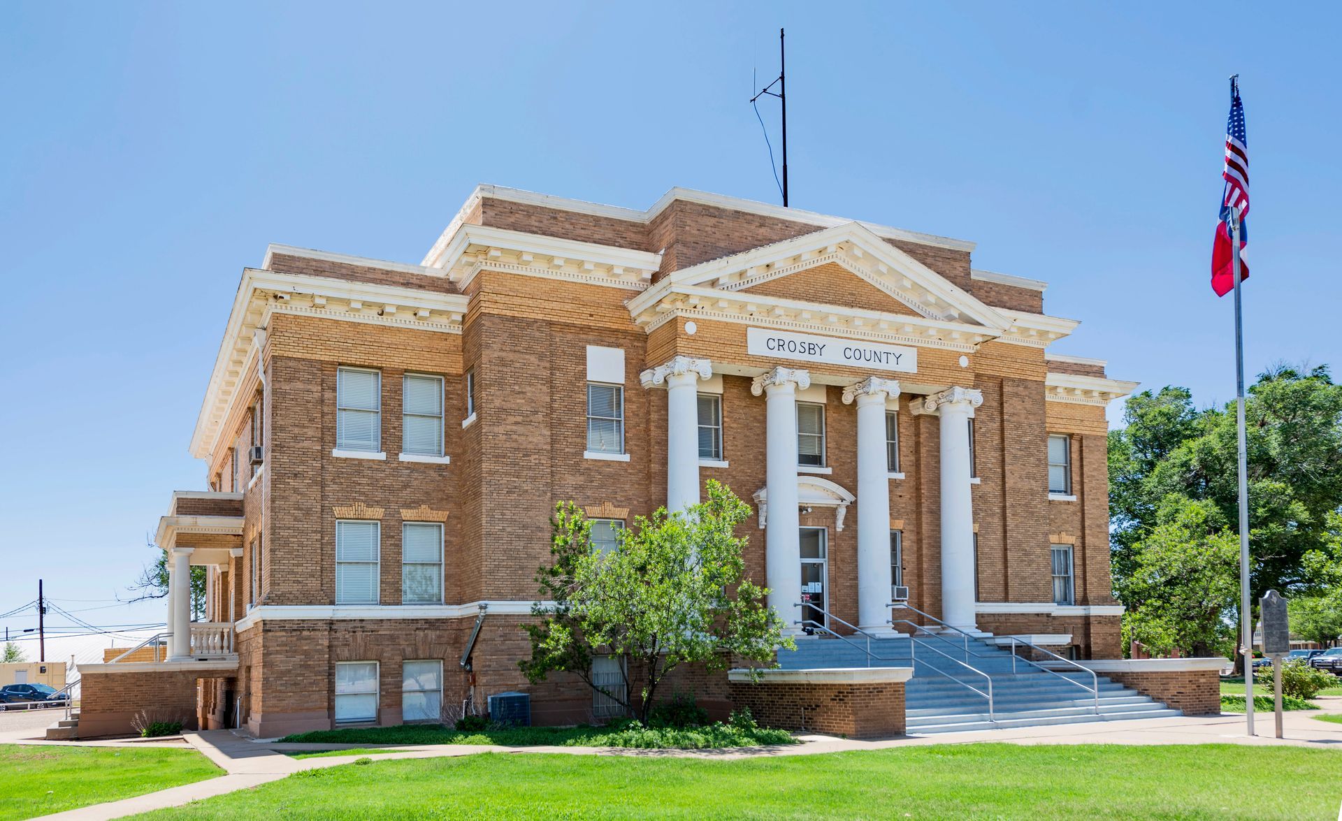 Historic brick courthouse with white columns and an American flag on a sunny day