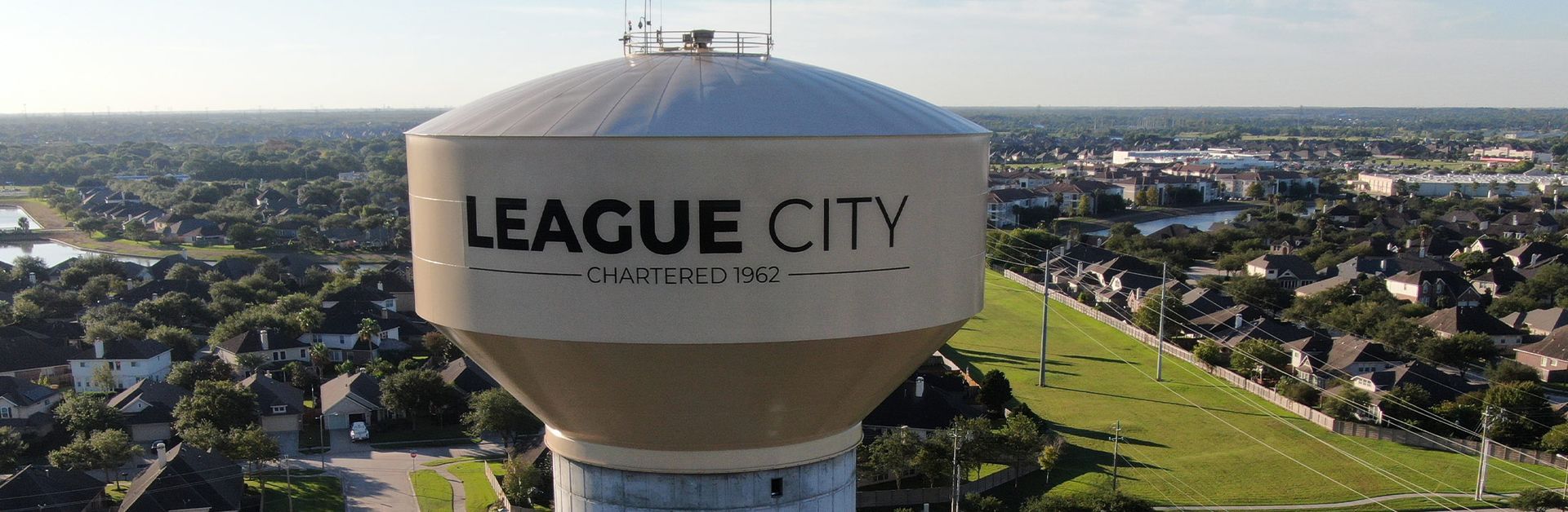 League City water tower above a suburban neighborhood under a clear sky
