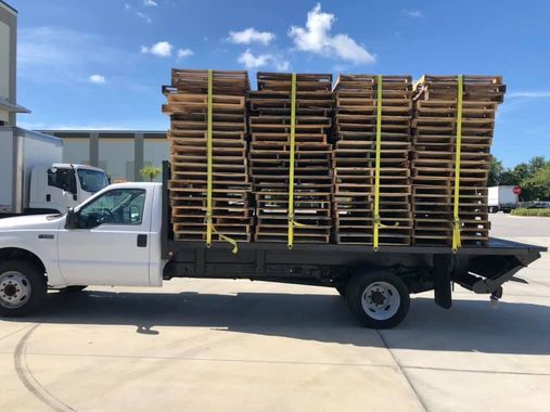 White flatbed truck loaded with stacked wooden pallets in a sunny industrial lot