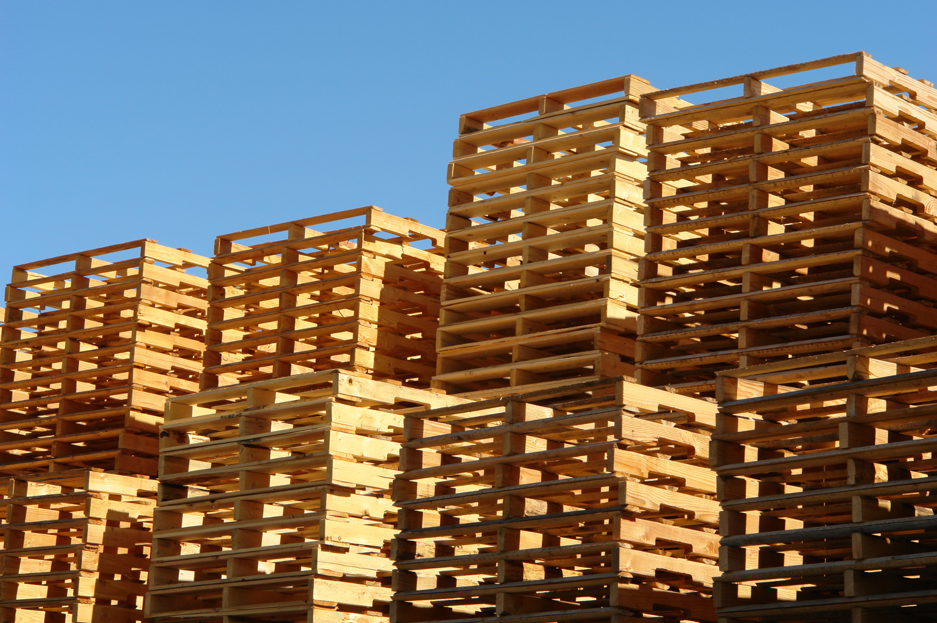 Stacked wooden pallets against a clear blue sky.