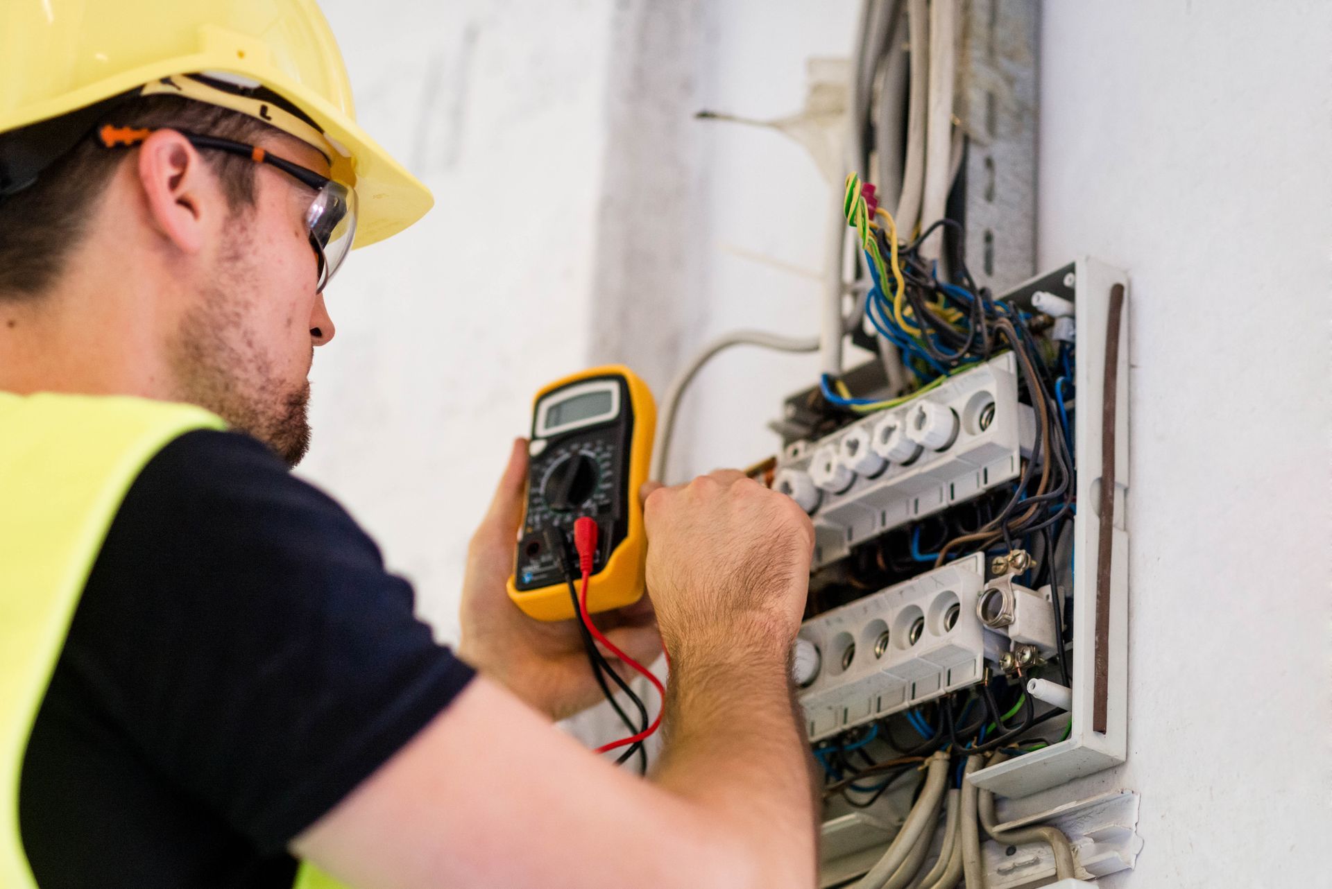 Electrician testing voltage at fuse box, showcasing electric services for safe wiring.
