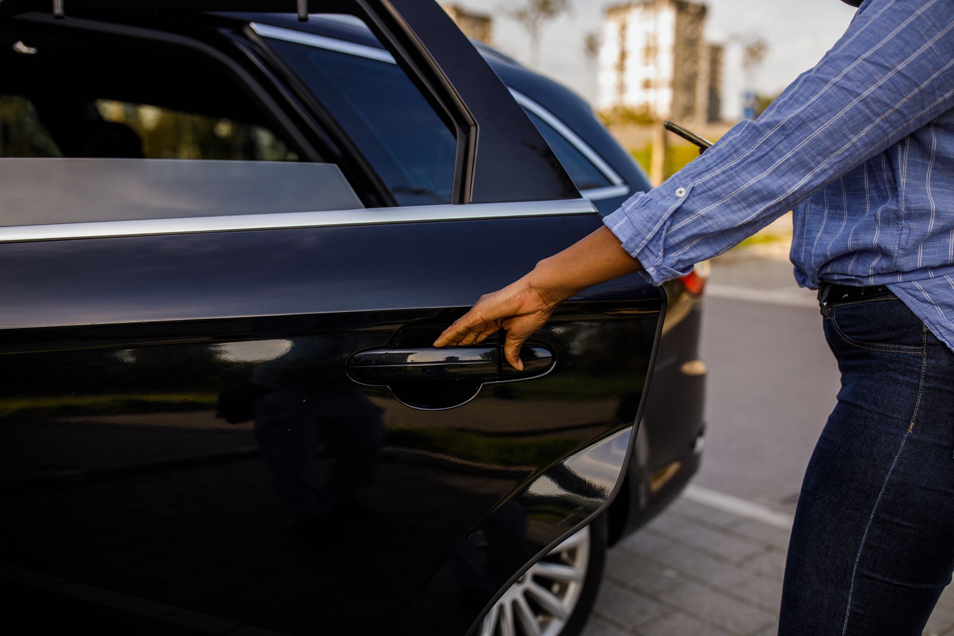 A woman is opening the door of a black car.