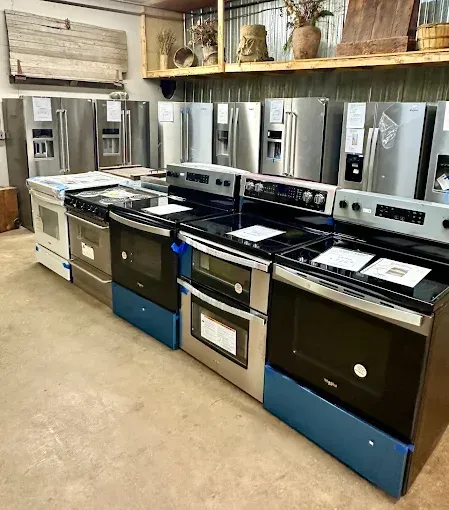 Appliance showroom with rows of stainless steel and black kitchen ranges and ovens on display.