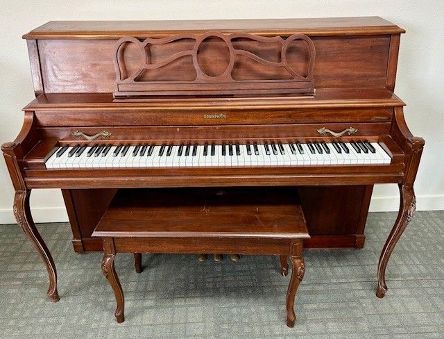 Vintage upright wooden piano with matching bench on a carpeted floor