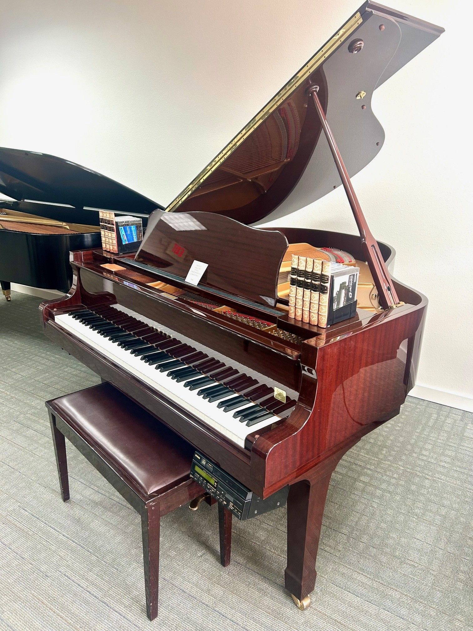 Brown grand piano with lid open and matching bench on a light floor