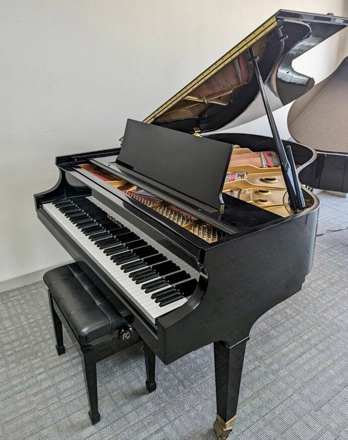 Black grand piano with matching bench in a bright room, lid open and keys visible