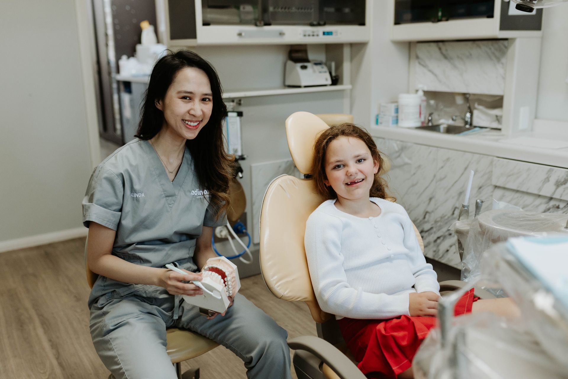 A dentist is sitting next to a little girl in a dental chair.