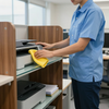 Person wiping a copier with a yellow cloth in an office copy room