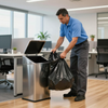 Man in blue polo placing a black trash bag into a stainless-steel office trash bin
