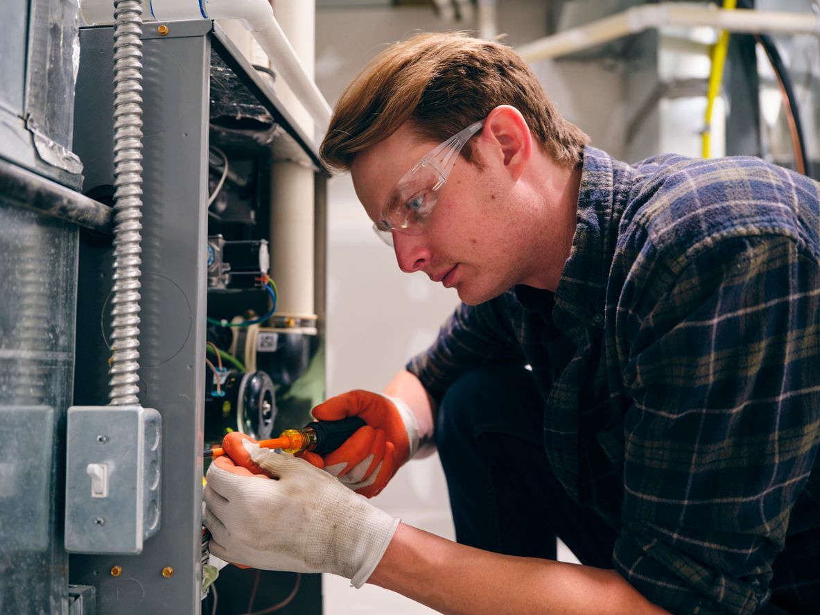 A photo of a repairman working inside a home and repairing a short cycling furnace