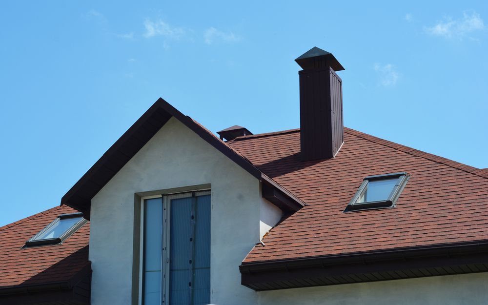 Red-tiled house roof with a chimney and skylight against a blue sky