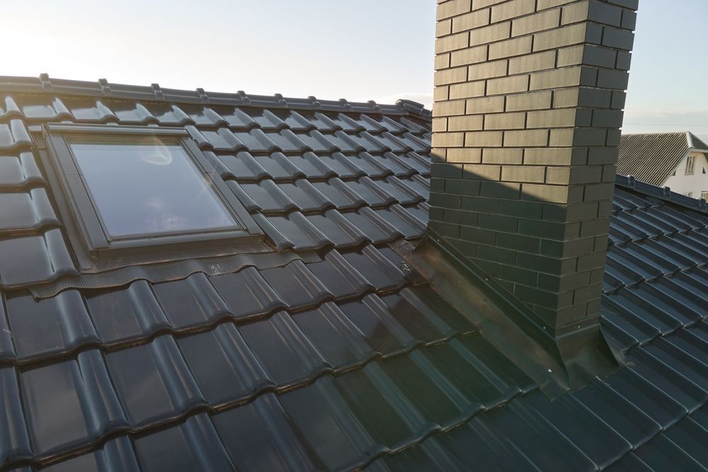 Roof with dark tiles, a skylight, and a brick chimney in sunlight