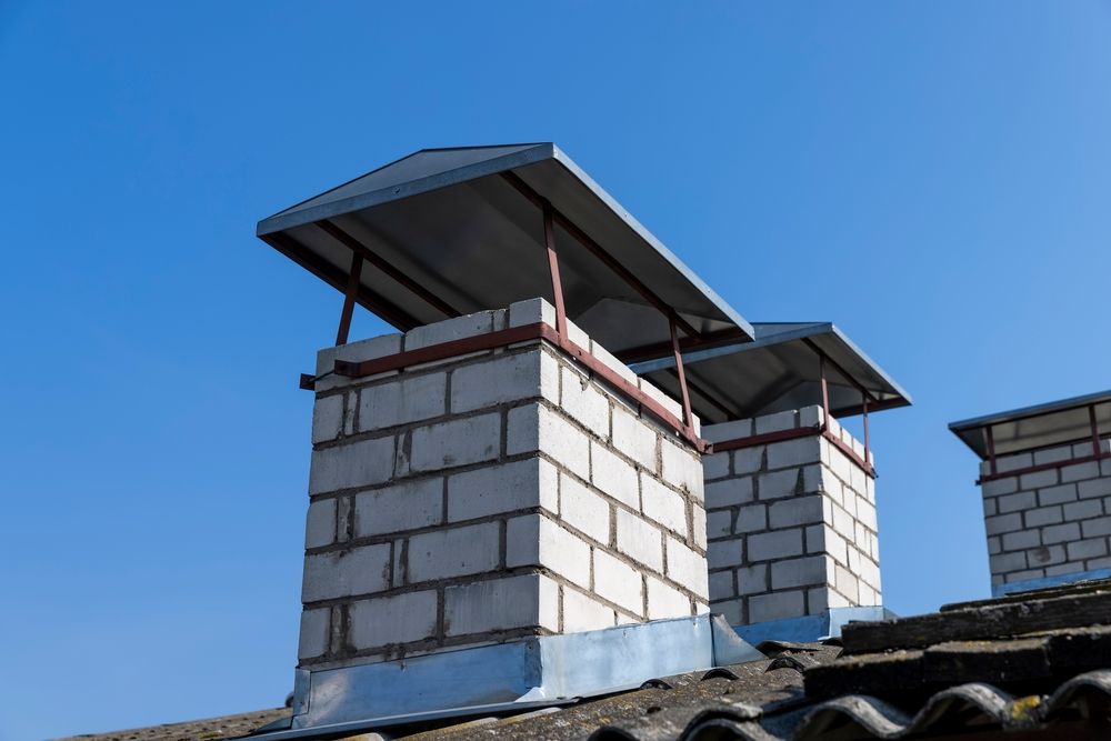 Brick rooftop chimneys with metal caps against a clear blue sky