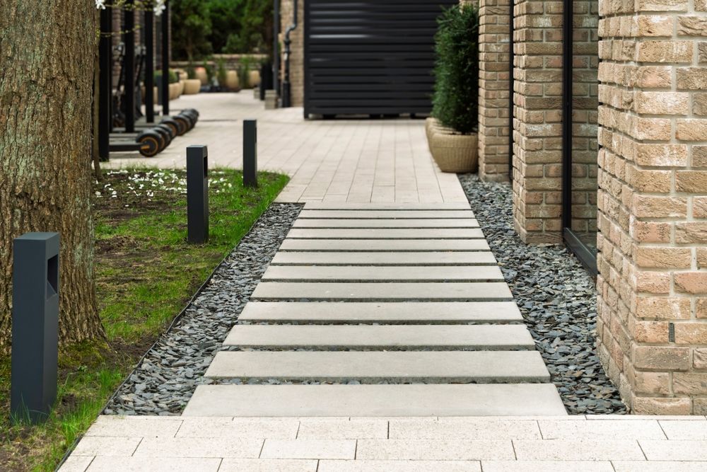 Modern stone walkway between brick walls with gravel borders and black bollards leading to a gate